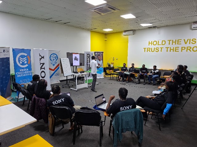 A photography training session with learners gathered around a demonstration